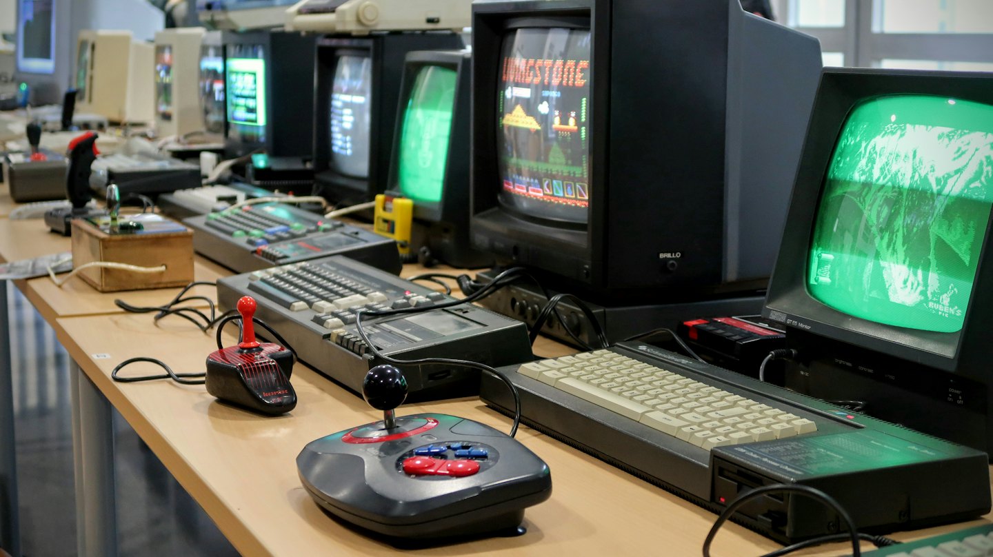 Vintage computers and gaming consoles arranged on a wooden table.